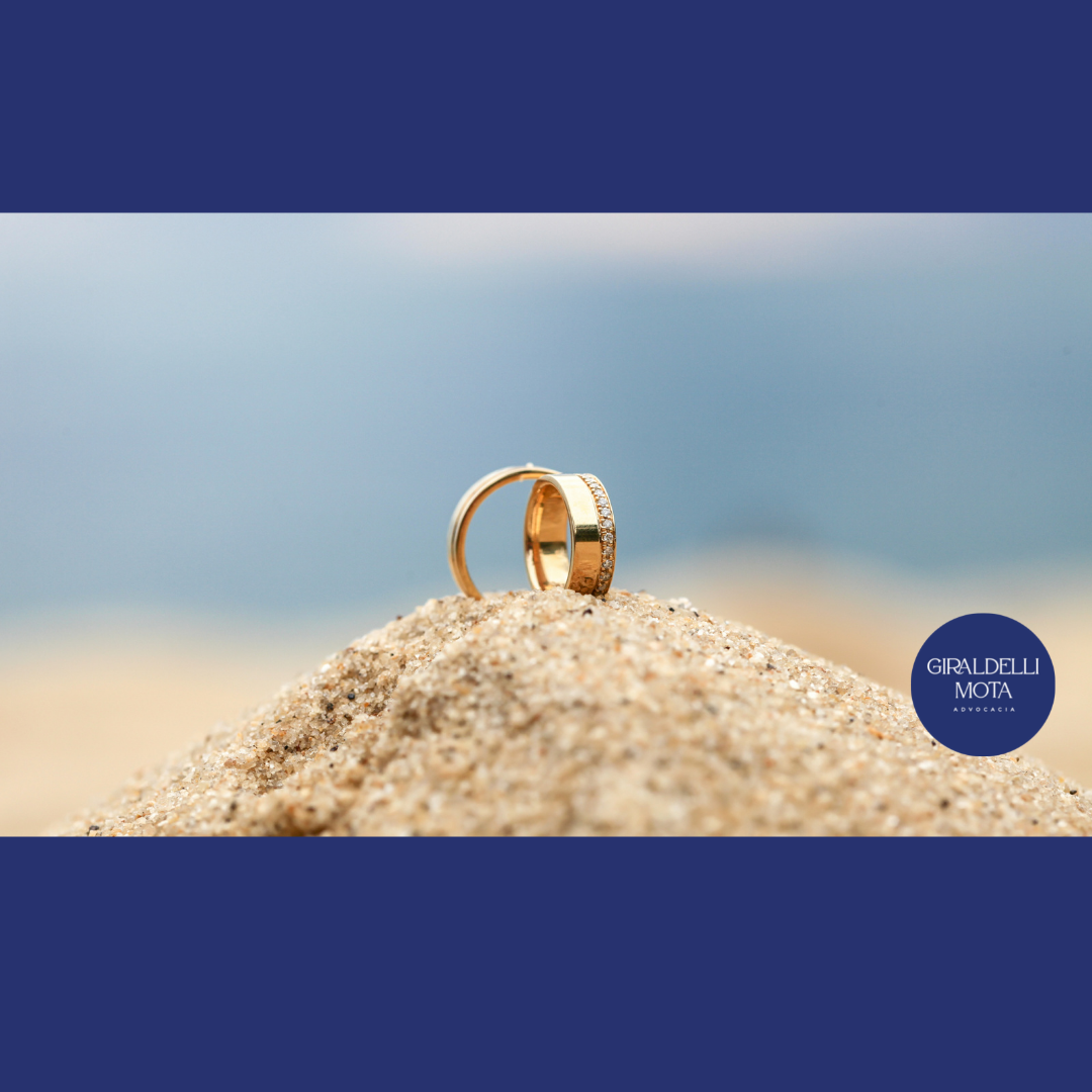 Foto de duas alianças no top de um monte de areia com o fundo azul similar a um oceano